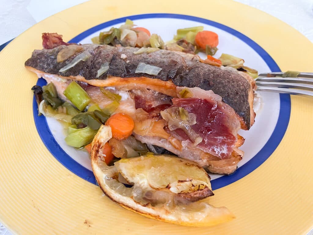 Truta assada com fatias de presunto e legumes, servida num prato