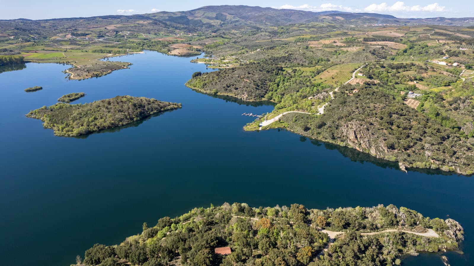 Vista aérea da albufeira do Azibo, com ilhas cobertas de mato e árvores, margens recortadas e a serra ao fundo