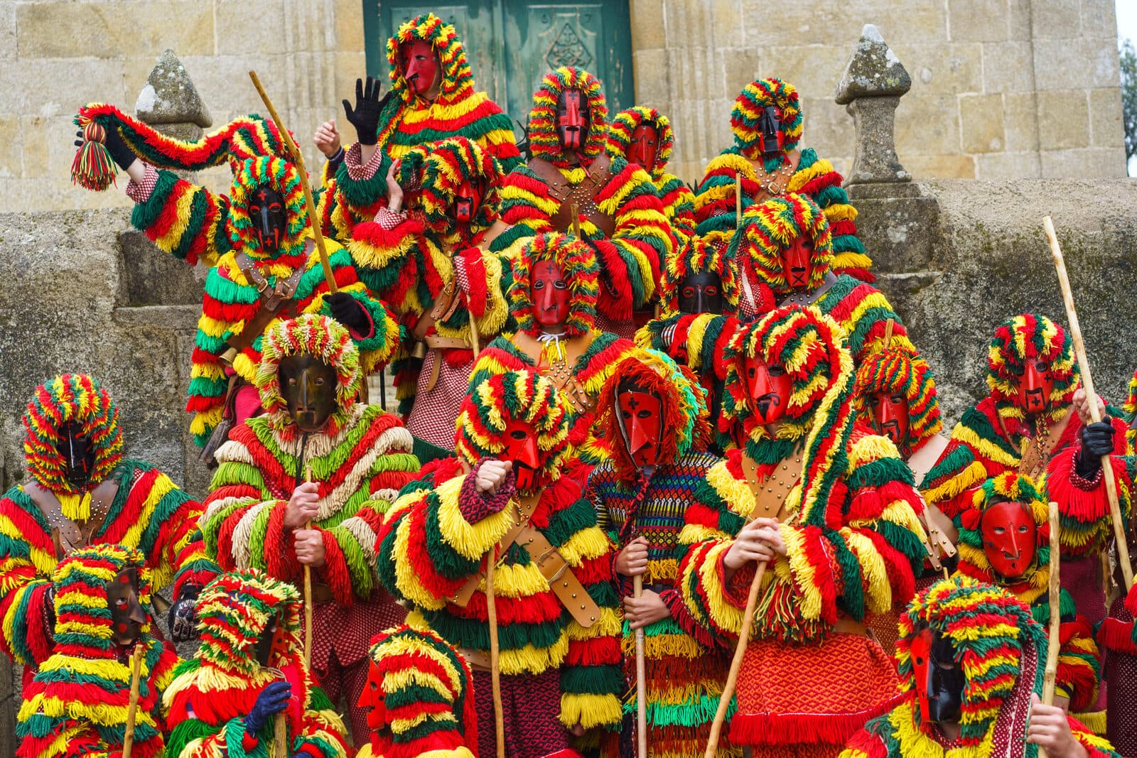 Grupo de caretos de Podence com máscaras vermelhas e fatos de franjas vermelhas, amarelas e verdes, nas escadas de uma igreja