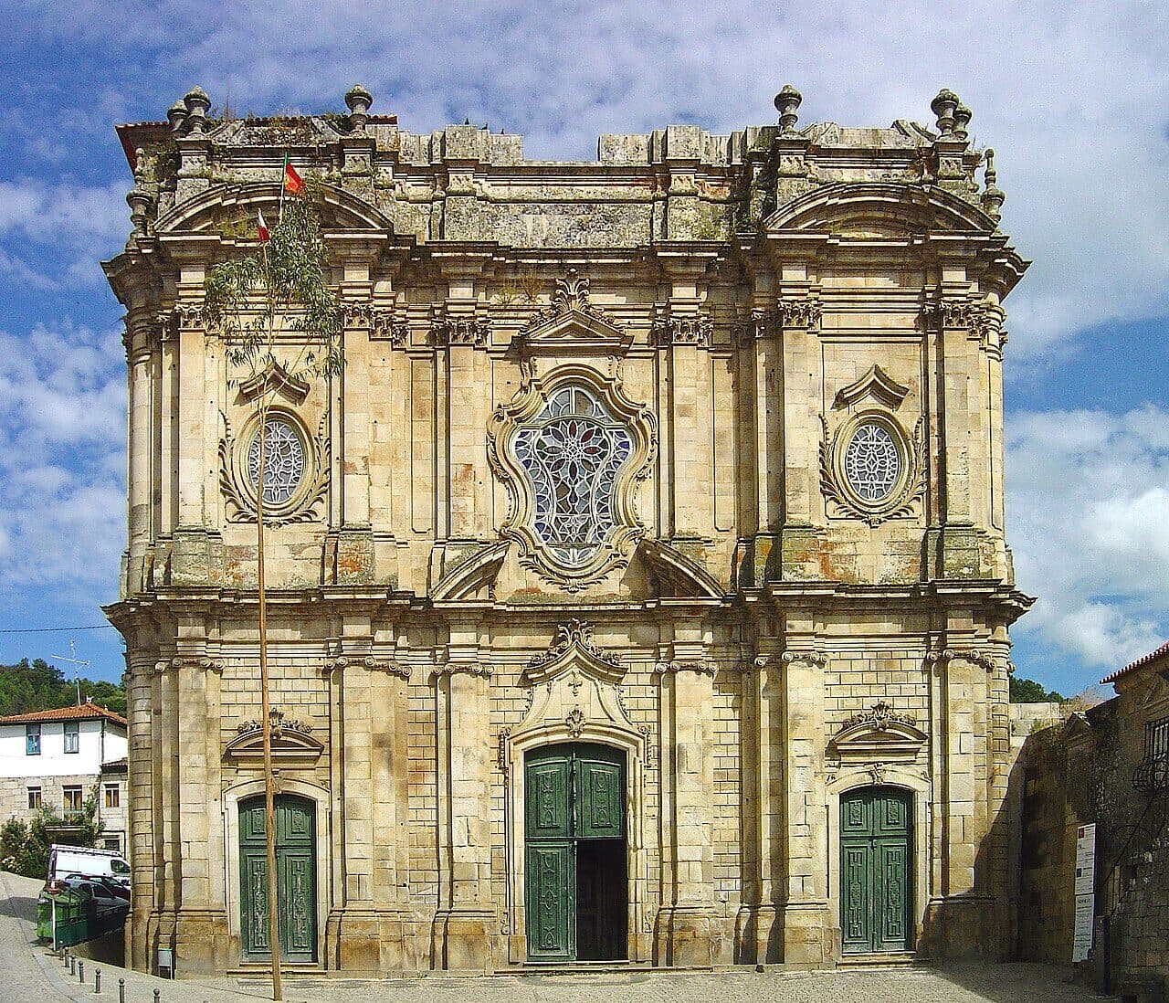 Fachada da igreja do Mosteiro de Salzedas, em pedra, com três portas verdes.