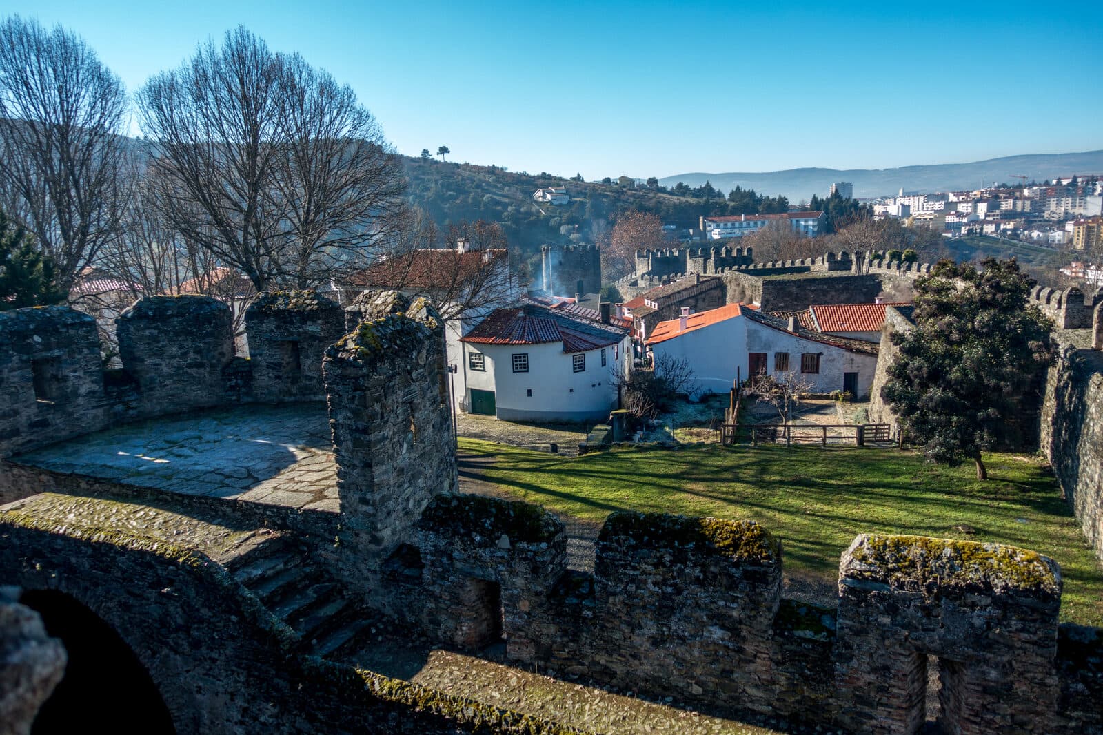 Muralhas da cidadela de Bragança com casas brancas de telhado vermelho e árvores sem folha, num dia de Inverno com céu limpo