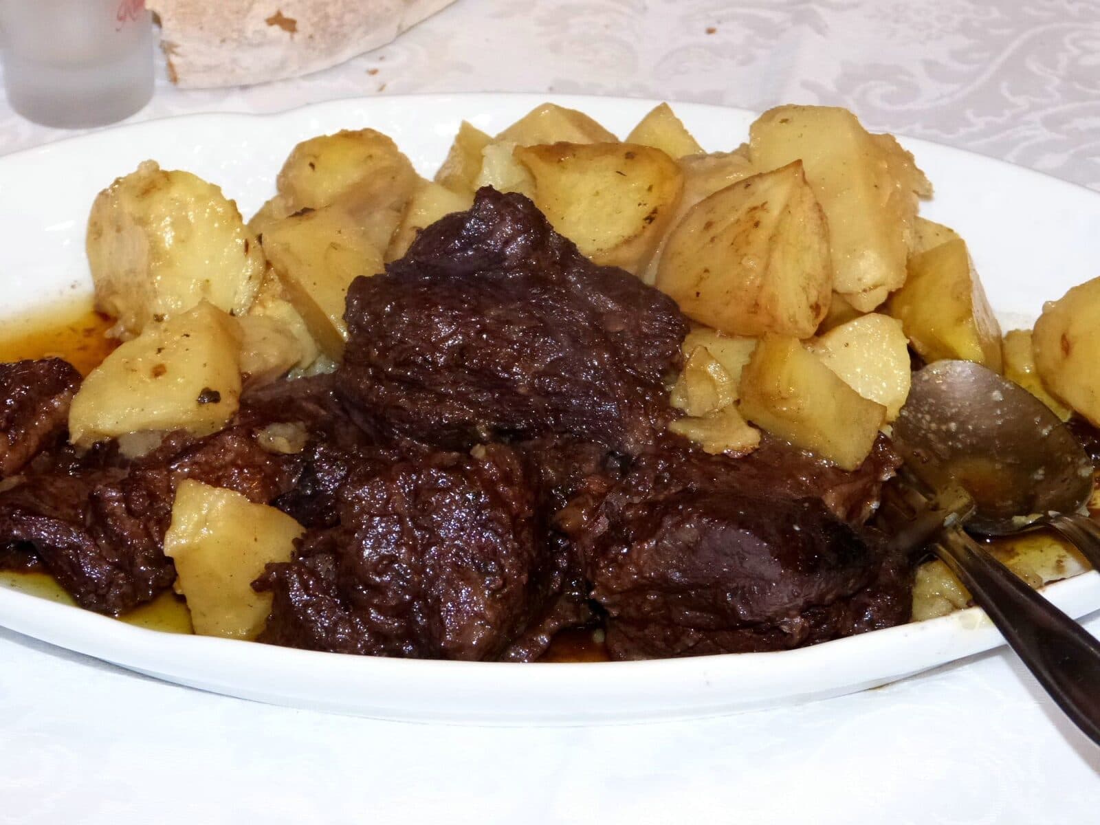 Pedaços de javali estufado com batatas, num prato oval, com molho escuro