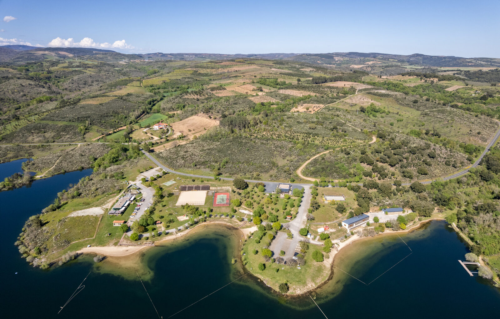 Vista aérea da praia da Fraga da Pegada, com o areal em meia-lua, o relvado, os campos de jogos e o parque de estacionamento numa península da albufeira