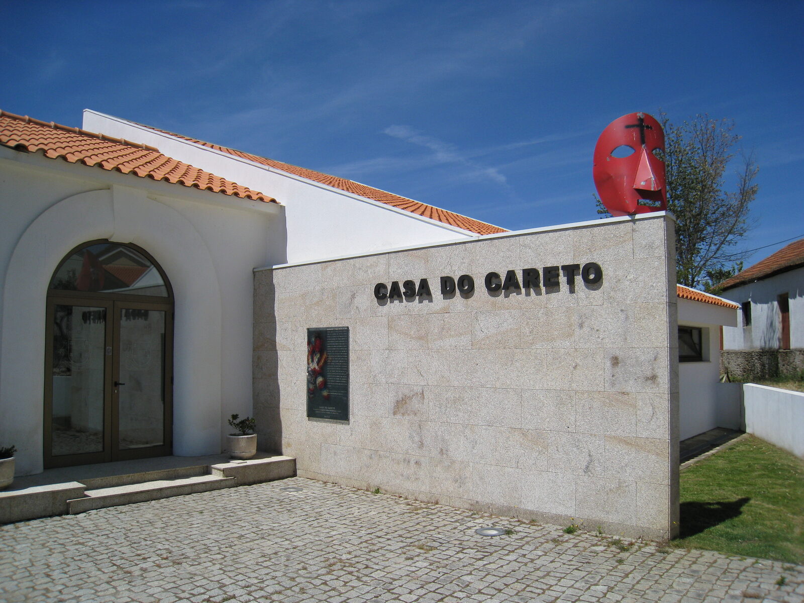 Edifício branco e de pedra da Casa do Careto, com o nome na fachada e uma máscara vermelha de careto sobre o telhado