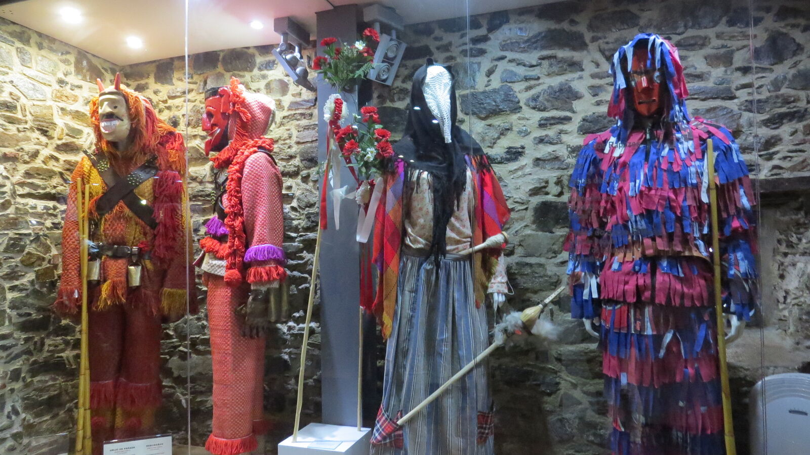Fatos de caretos e máscaras expostos numa sala de paredes de pedra