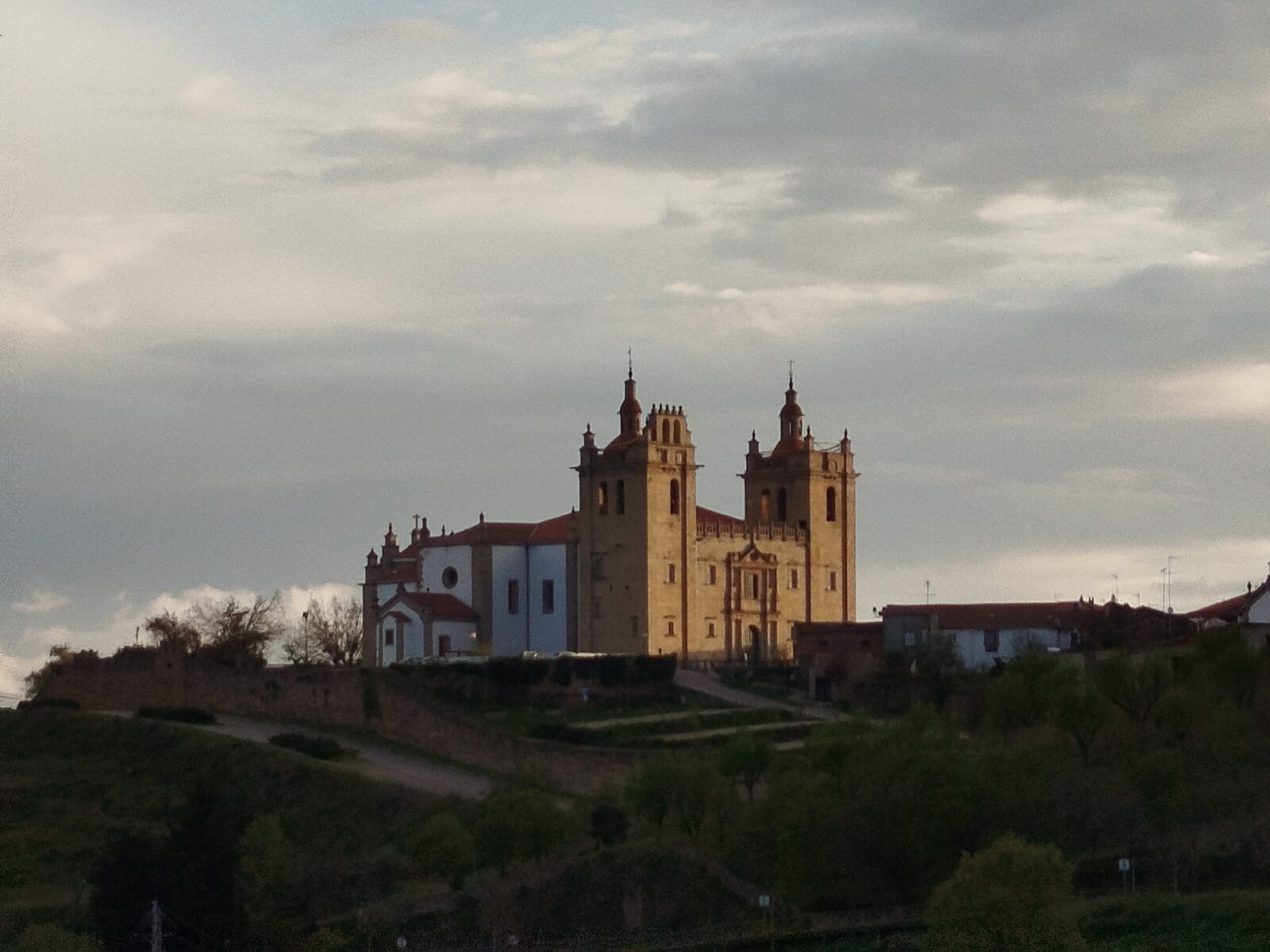 A Sé de Miranda do Douro, com as duas torres iluminadas pelo sol do fim da tarde, no alto da cidade sobre a encosta