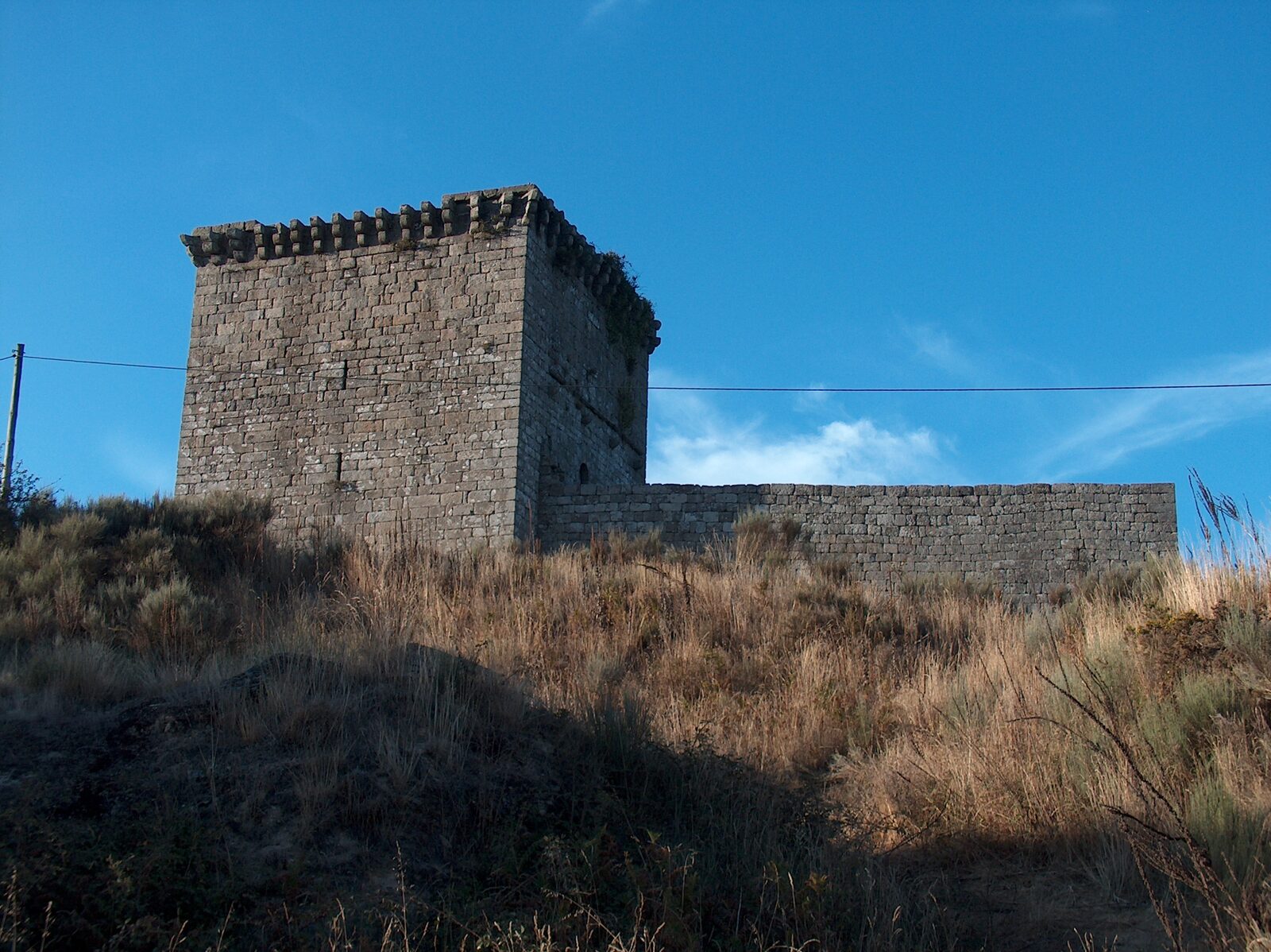 Torre de menagem e muralha do castelo de Monforte, em granito, no alto de uma encosta com mato seco