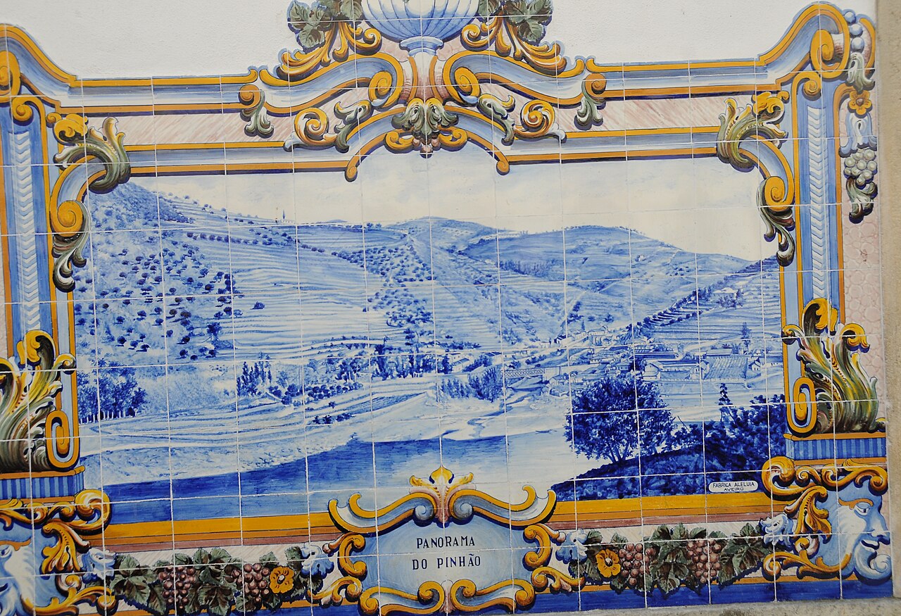Painel de azulejos azuis e brancos com moldura amarela, com a vista do vale do Douro no Pinhão e a legenda "Panorama do Pinhão"