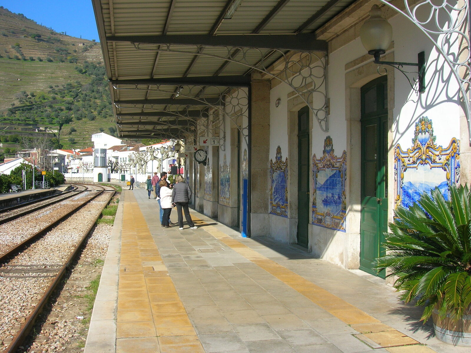 Plataforma da estação do Pinhão, com painéis de azulejos azuis e brancos na fachada e a linha de comboio ao lado