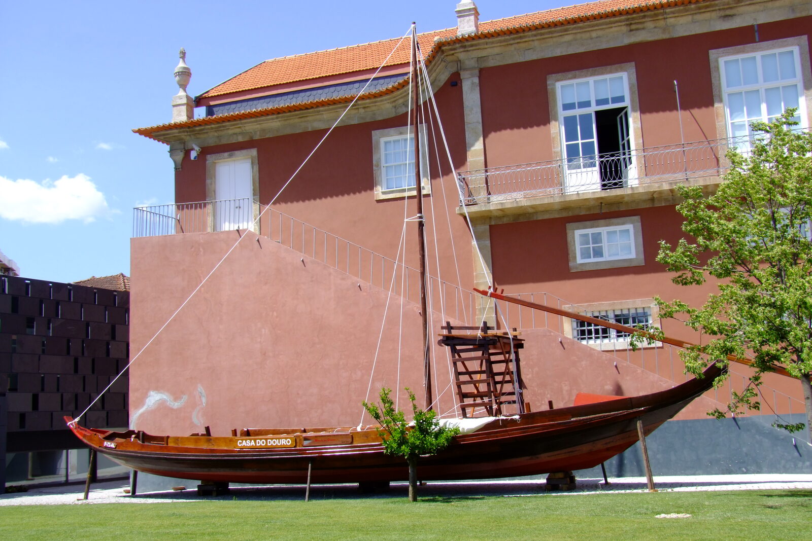 Edifício da Casa da Companhia, de paredes cor de tijolo, com um barco rabelo exposto no relvado em frente