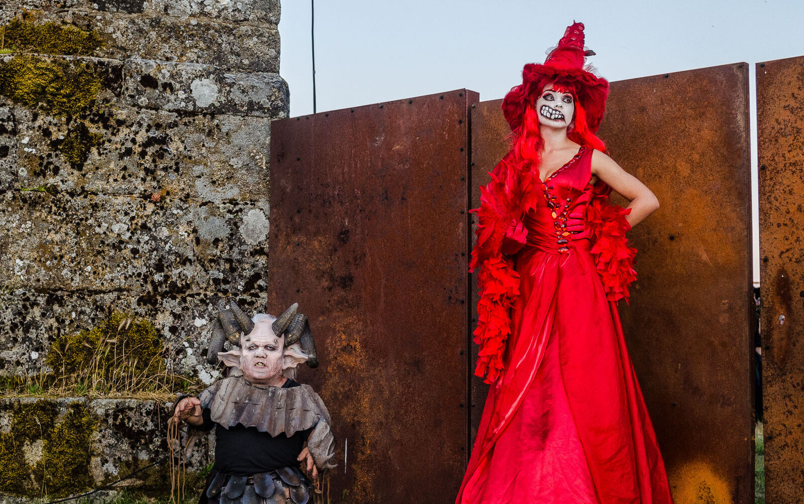 Duas personagens caracterizadas, uma bruxa de vestido vermelho e um demónio com chifres, junto às muralhas do castelo