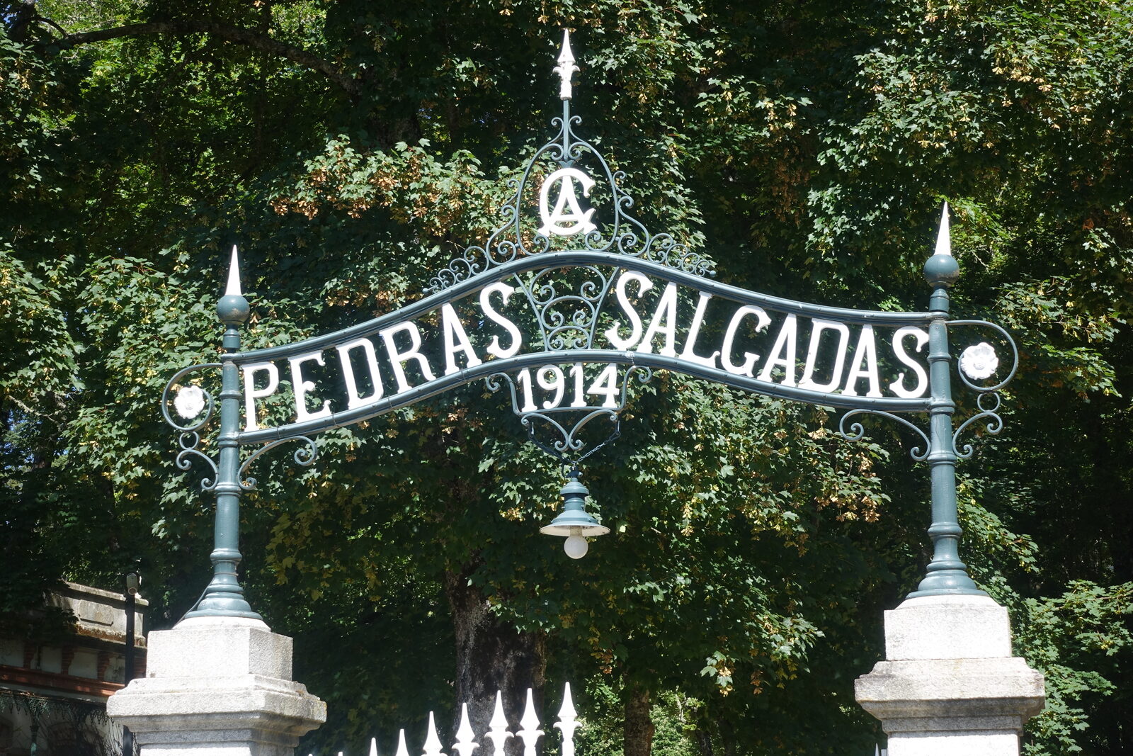 Portão de ferro forjado com a inscrição Pedras Salgadas 1914, entre árvores